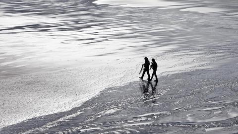 Zwei Menschen spazieren am leeren Strand.