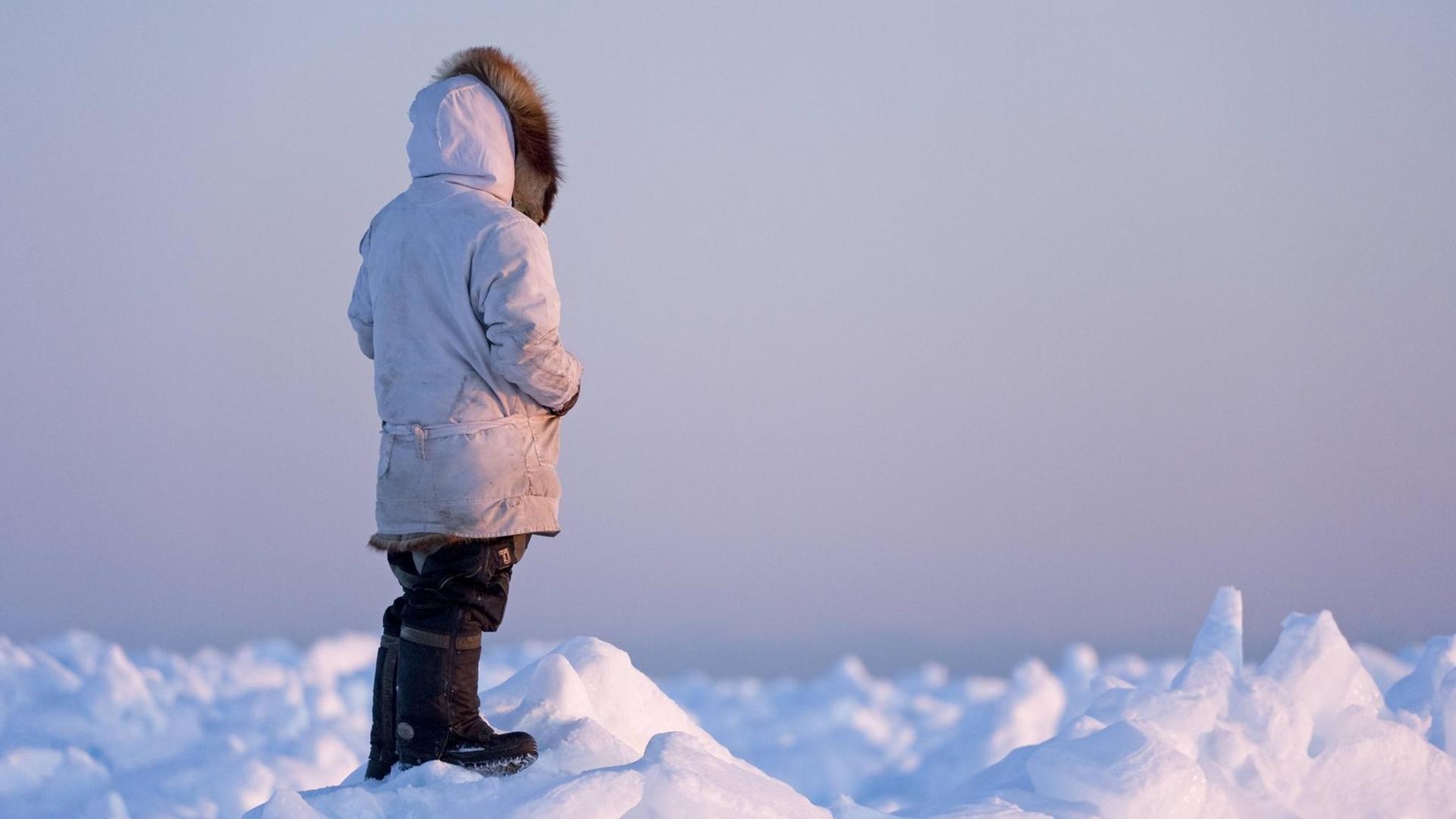 Ein Mann des Inupiaq steht auf dem Eis und schaut aufs Eis.