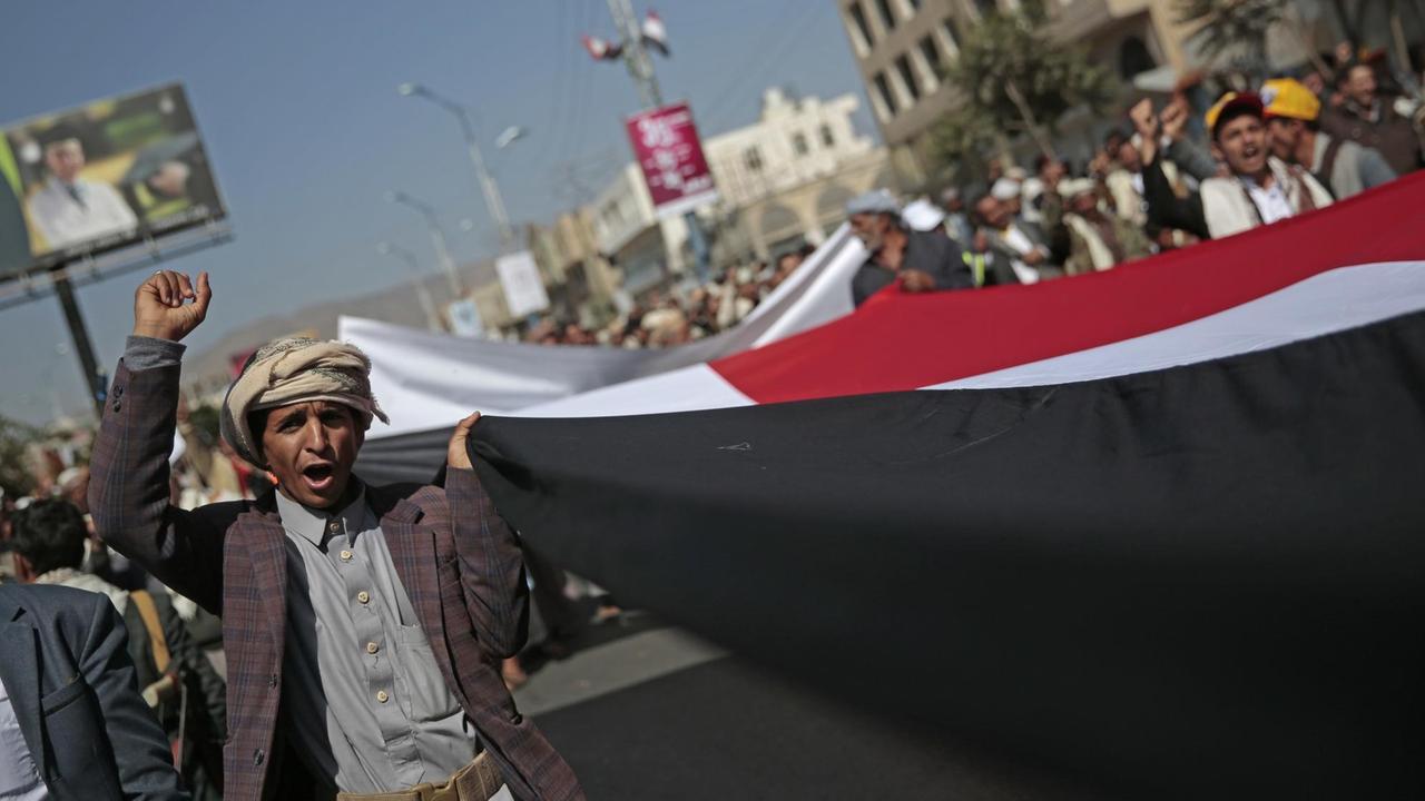 Ein Demonstrant trägt am 13.11.2017 in Sanaa (Jemen) bei einem Protest, auf dem die Öffnung der Flug- und Seehäfen in dem Land gefordert wird, eine riesige jemenitische Flagge. Ein von Saudi-Arabien geführtes Bündnis fliegt im Jemen Luftangriffe gegen Huthi-Rebellen. Die Koalition hatte in der vergangenen Woche die Flug- und Seehäfen geschlossen. Hilfsorganisationen warnten jedoch, dem Land drohe durch die Blockade eine der größten Hungerkatastrophen weltweit.