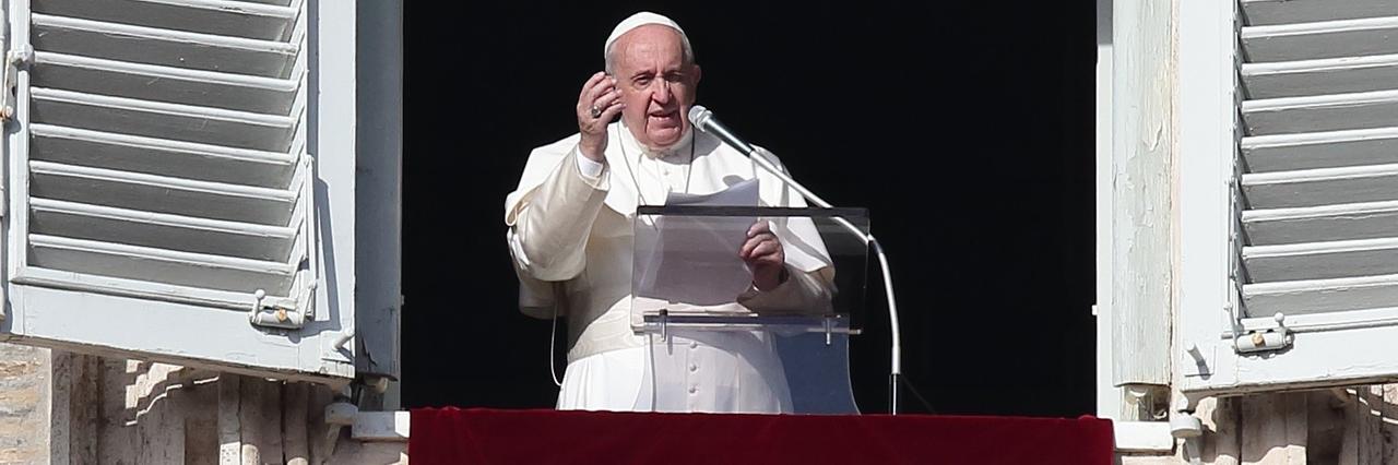 Papst Franziskus während des Angelus-Gebets auf dem Petersplatz. Er steht am offenen Fenster und hebt die rechte Hand (2019).