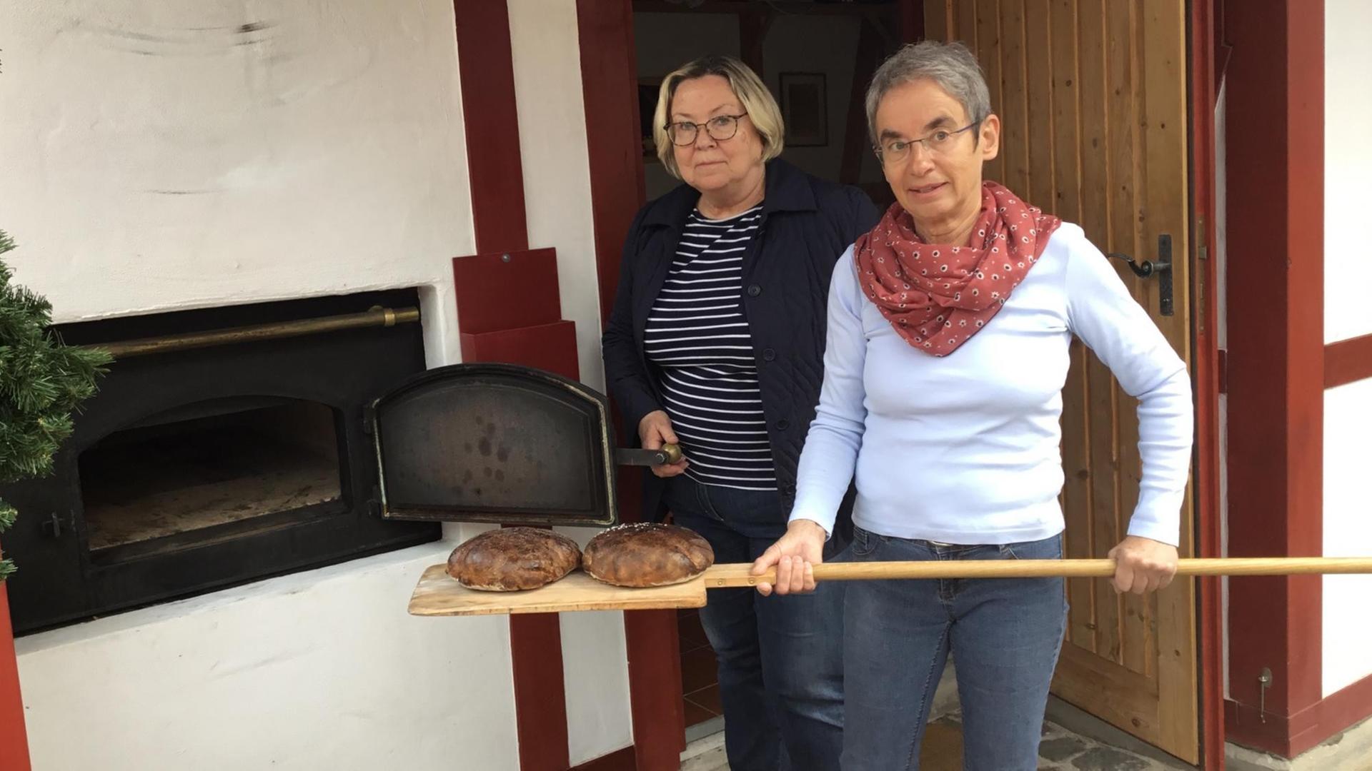 Die Hobby-Bäckerinnen Maria Schwarze-Kaufmann (rechts) und Sigrid Schindler holen die Brote aus dem Elektro-Ofen im Backhaus Bobenheim am Berg (Pfalz)