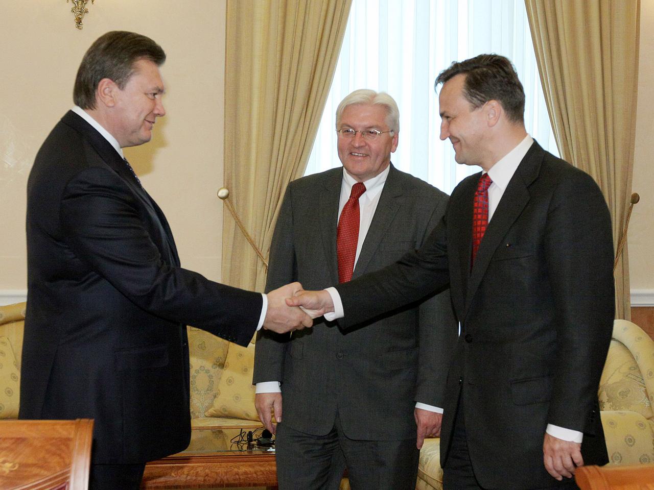 Der ukrainische Präsident Viktor Janukowitsch schüttelt dem polnischen Außenminister Radoslav Sikorski die Hand, dahinter steht der deutsche Außenminister Frank-Walter Steinmeier.