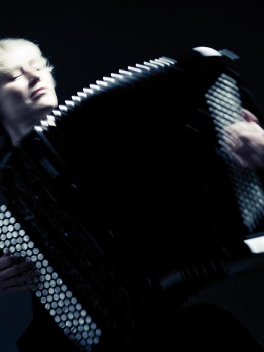 Musikerin spielt Knopfakkordeon in einem schwarzen Raum