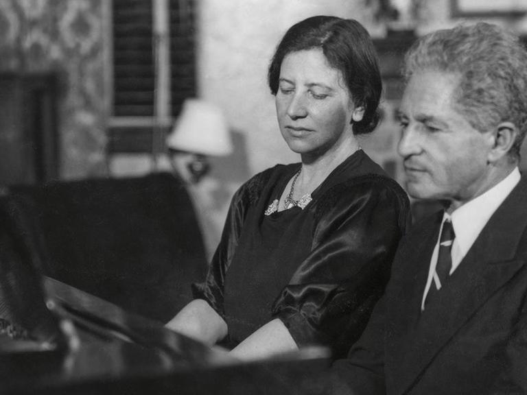 Auf dem schwarz/weiß Foto ist ein Mann und eine Frau zu sehen, die gemeinsam Klavier spielen