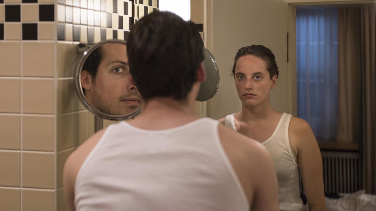Ein Mann steht vor einem Spiegel. Im Spiegelbild sieht man eine Frau.