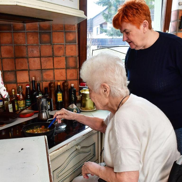 Pflegebedürftige im Rollstuhl in der Küche mit einer Pflegekraft. 