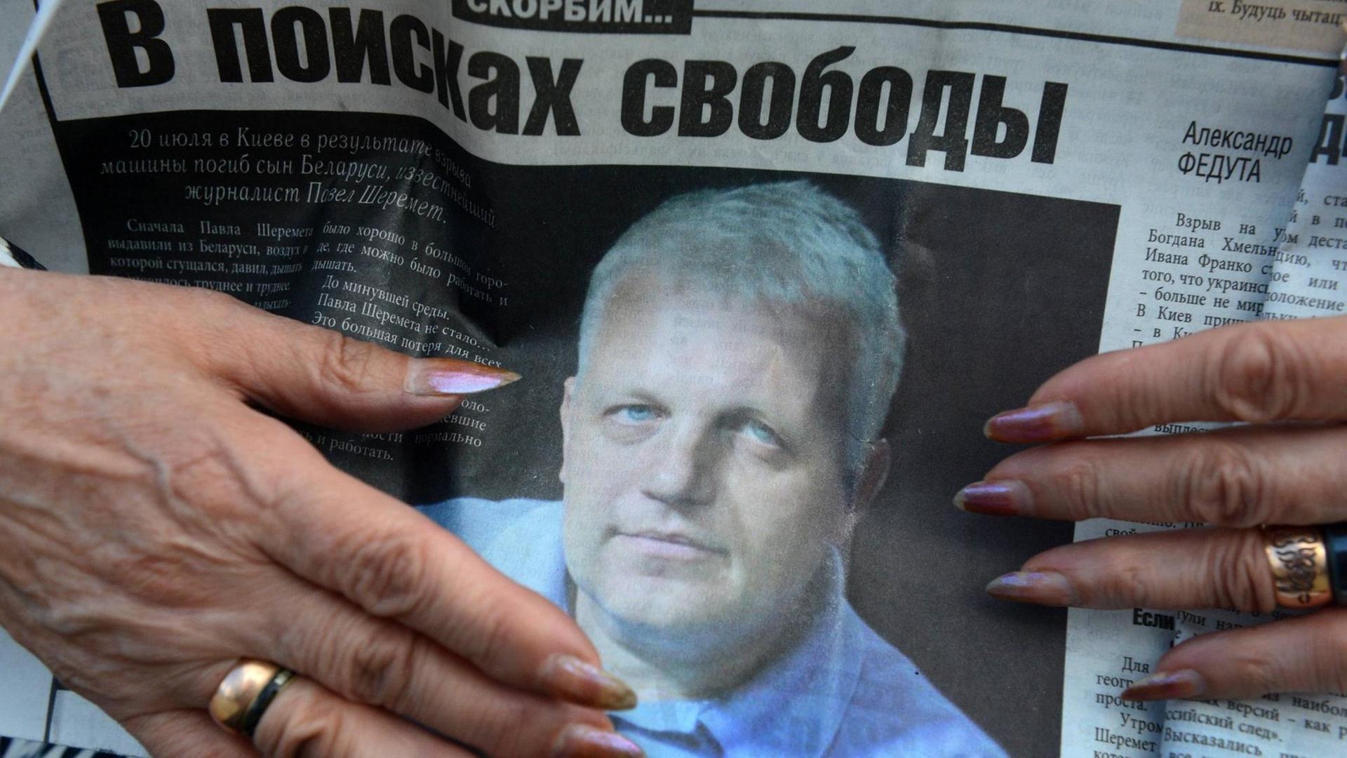 Eine Person hält eine Zeitung mit dem Photo des ermordeten Journalisten Pawel Scheremet während seiner Beerdigung am 23. Juli 2016 auf dem Severnoye Friedhof in Minsk, Weißrussland.