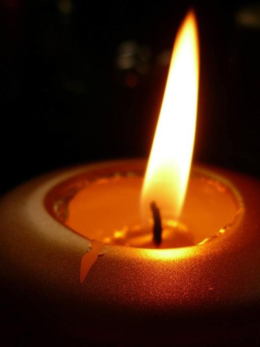 Brennende Kerze vor schwarzem Hintergrund