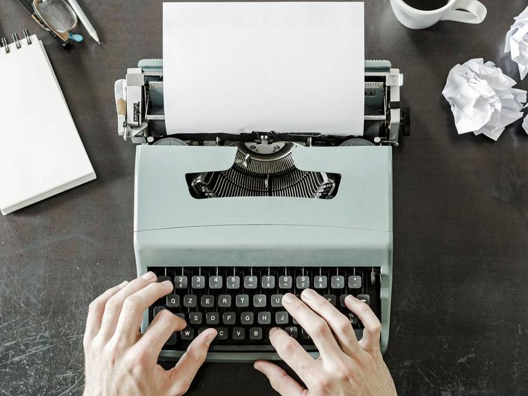 Ein Mann sitzt vor dem weißen Blatt an einer Schreibmaschine.
