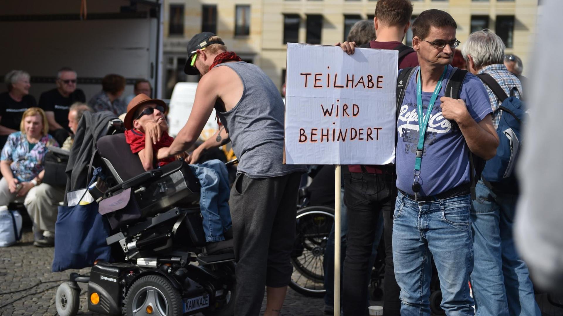 Ein Mann lehnt sich an ein Schild mit dem Schriftzug "Teilhabe wird behindert" auf dem Pariser Platz in Berlin.