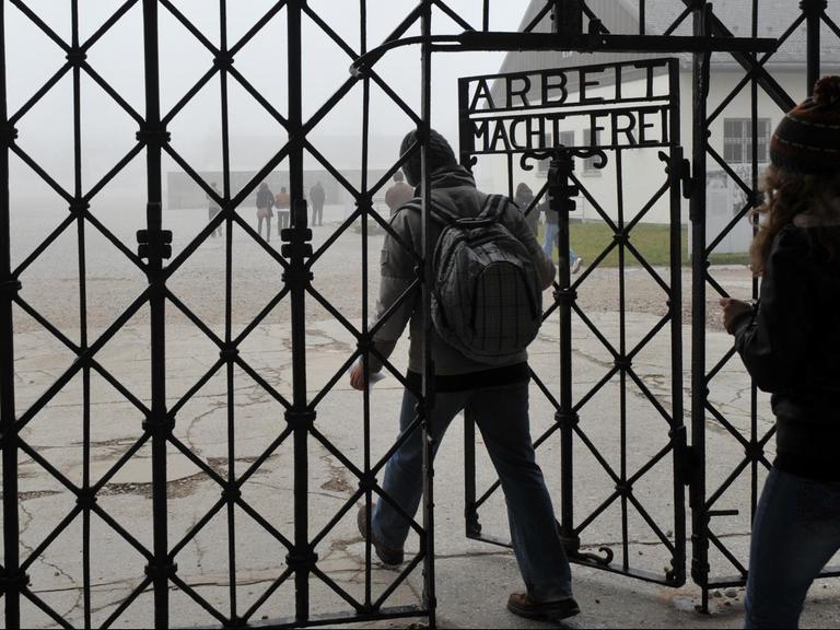 "Arbeit macht frei" steht am 19.11.2012 an einem Tor zum ehemaligen Konzentrationslager in Dachau nahe München. Zwei Menschen gehen nacheinander hindurch.