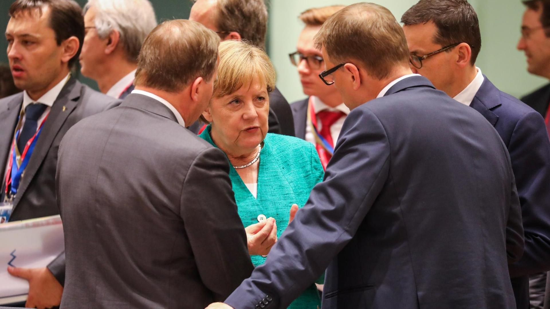 Merkel im Gespräch mit zwei Männern, die nur von hinten zu sehen sind.