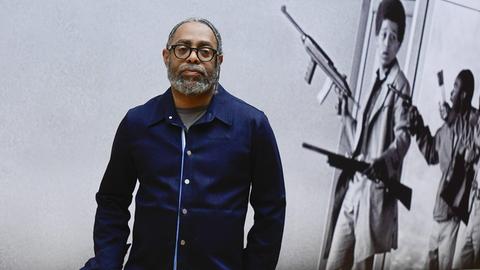 Künstler Arthur Jafa posiert vor einer Fotografie mit bewaffneten Männern