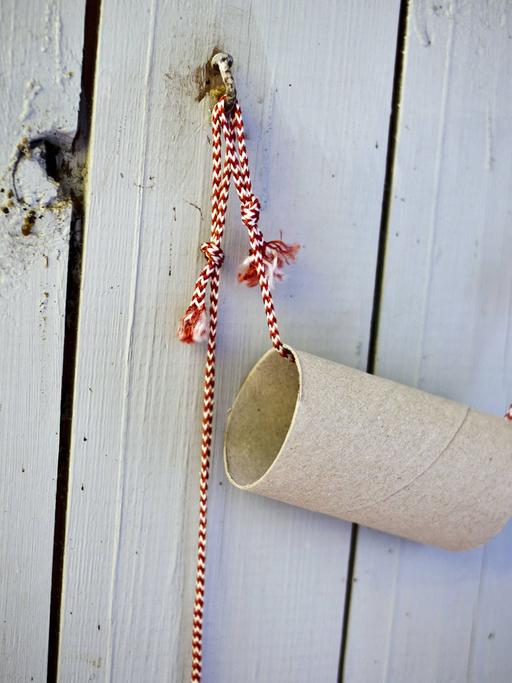 Eine leere Rolle Toilettenpapier hängt an einem rot-weißen Band an einer Bretterwand.