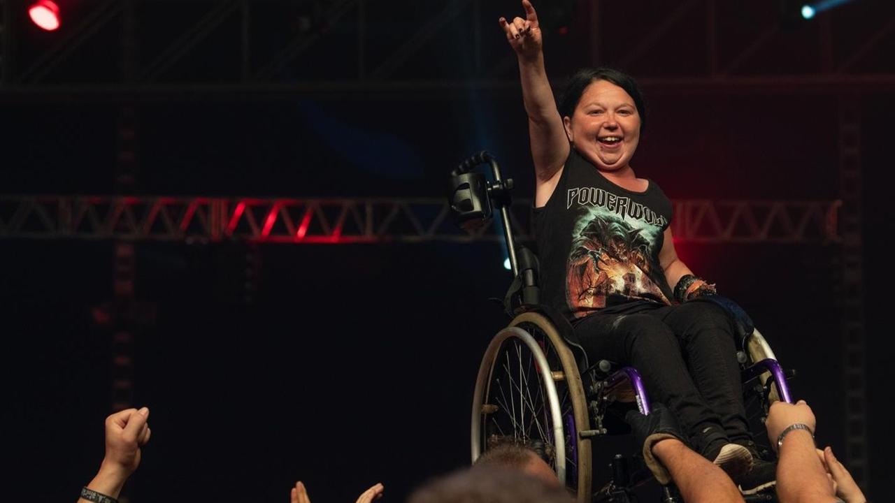 Wacken Open Air 2018, Frau im Rollstuhl steht am Bühnenrand vor begeistertem Publikum, im Hintergrund eine dunkle Bühne