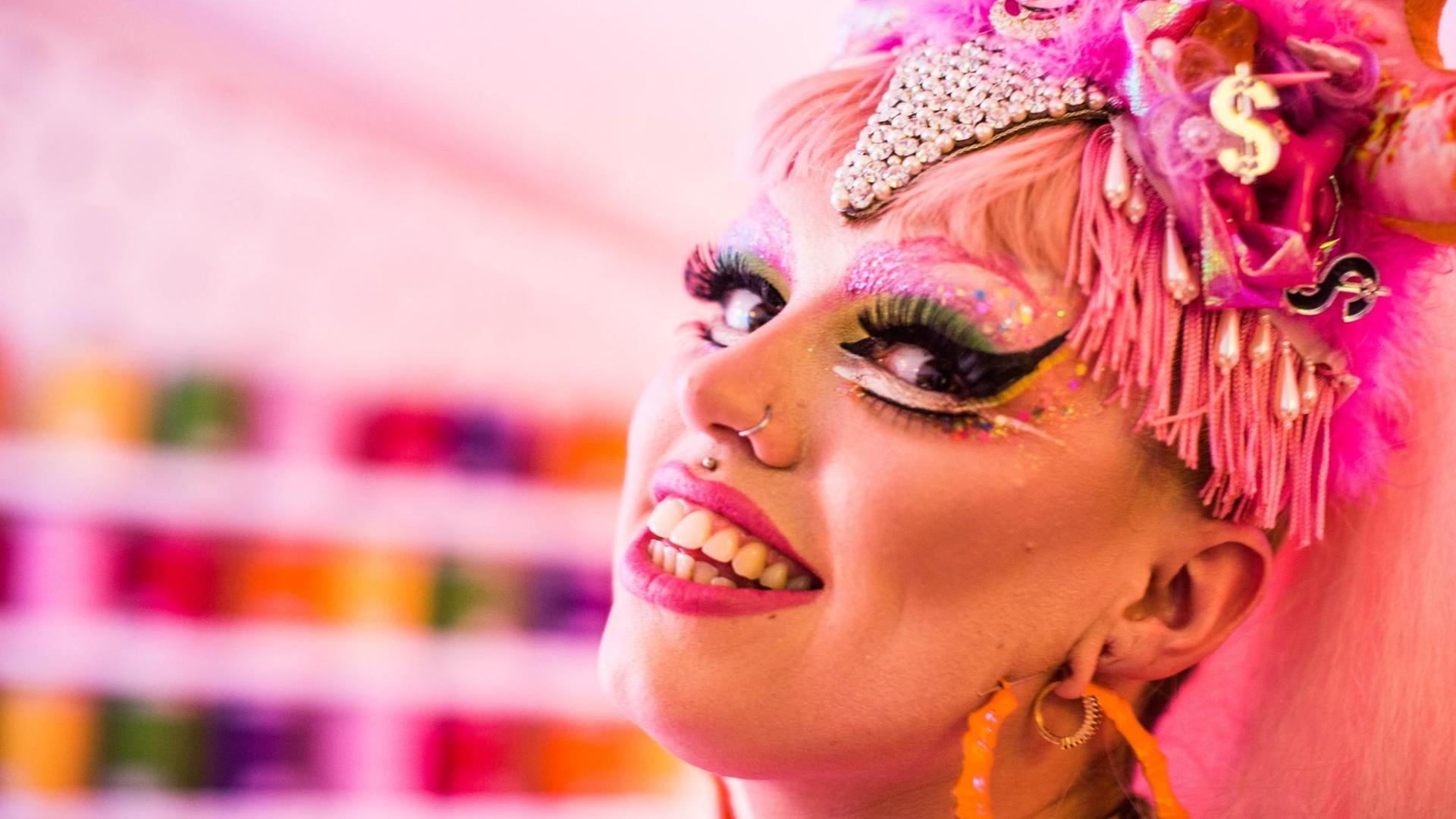 Mit einem Lächeln auf den Lippen, blick eine gestylte Drag Queen in die Kamera.