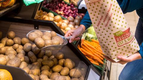 Jemand füllt in einem Supermarkt lose Kartoffeln in eine Papiertüte