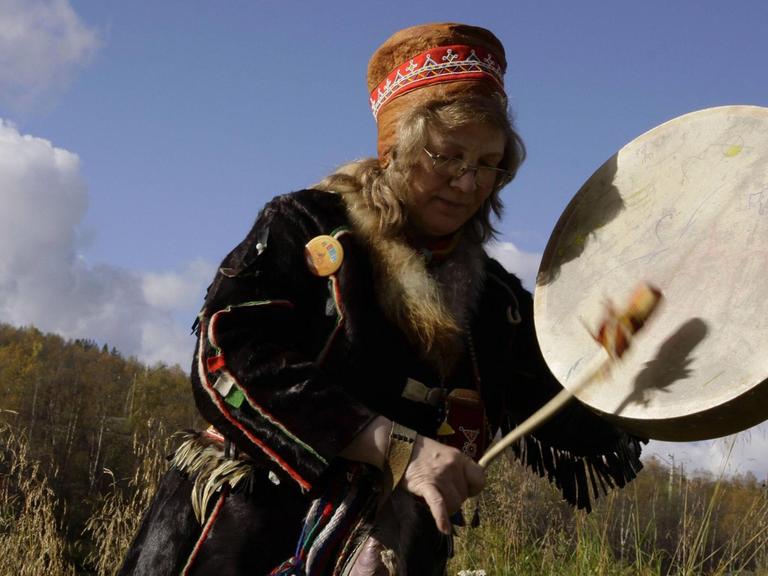 Schamanin in traditioneller samischer Kleidung beim Trommeln.