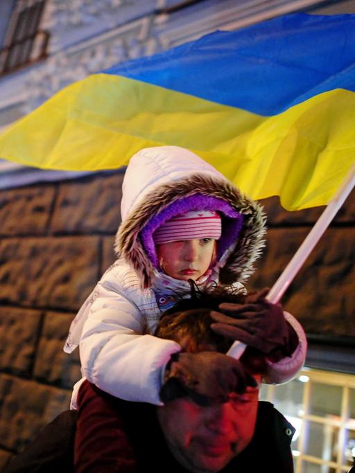 Vater trägt sein Kind, das in der Hand eine ukrainische Flagge hält, bei Protesten in Kiew am 30.11.2013