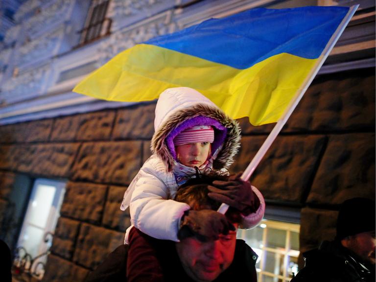 Kind mit ukrainischer Flagge auf der Schulter seines Vaters