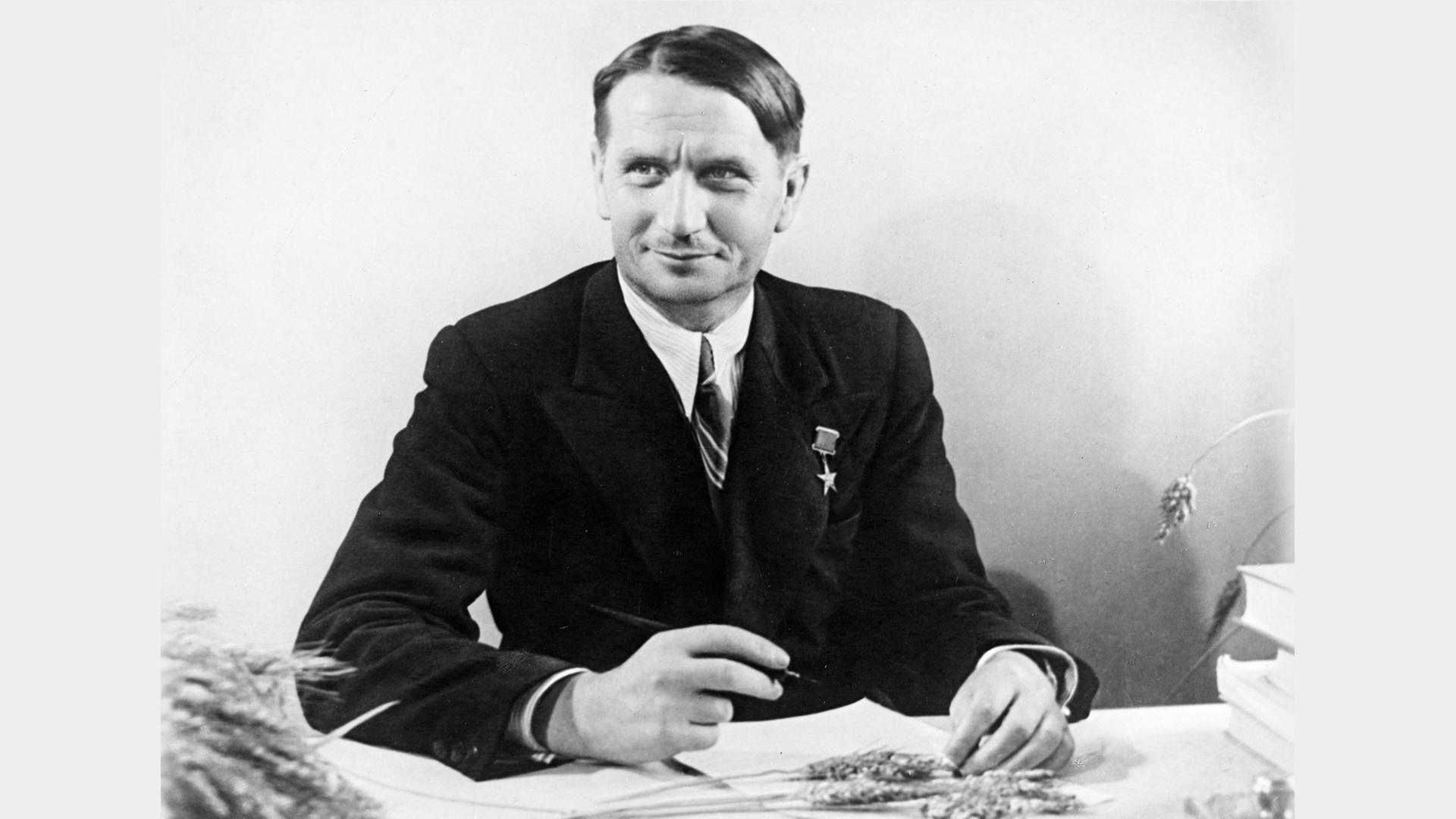 Trofim Denissowitsch Lyssenko (1898-1976) sitzt am Schreibtisch, auf dem Getreideähren liegen (Foto)
