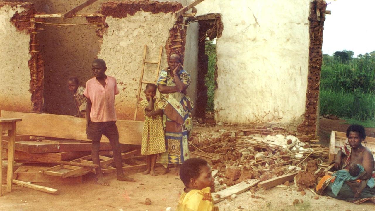 Ein zerstörtes Haus nach der Vertreibung der Dorfbewohner in Mubende 2001. Die Mauern sind eingerissen. Kinder und Frauen gucken fassungslos.