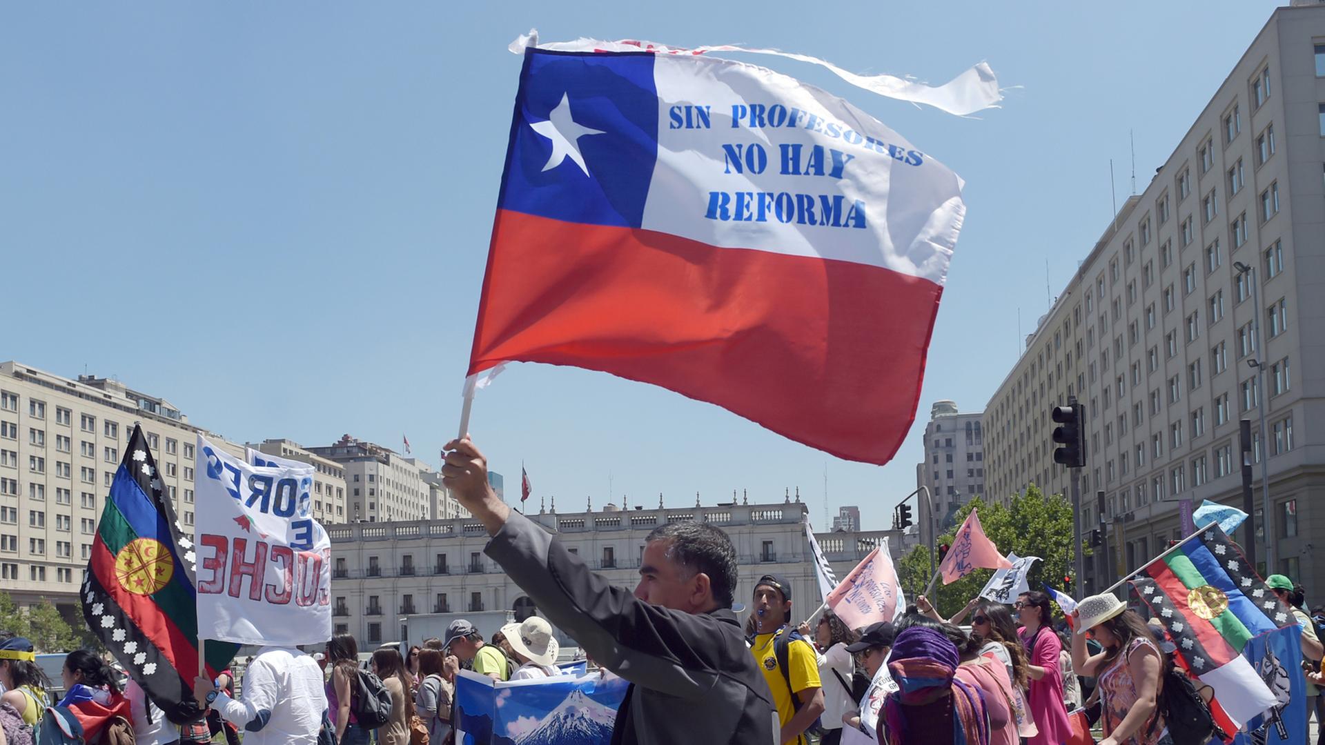 Demonstranten auf einer Straße, einer schwenkt die chilenische Flagge mit der Aufschrift "Sin profesores no hay reforma"