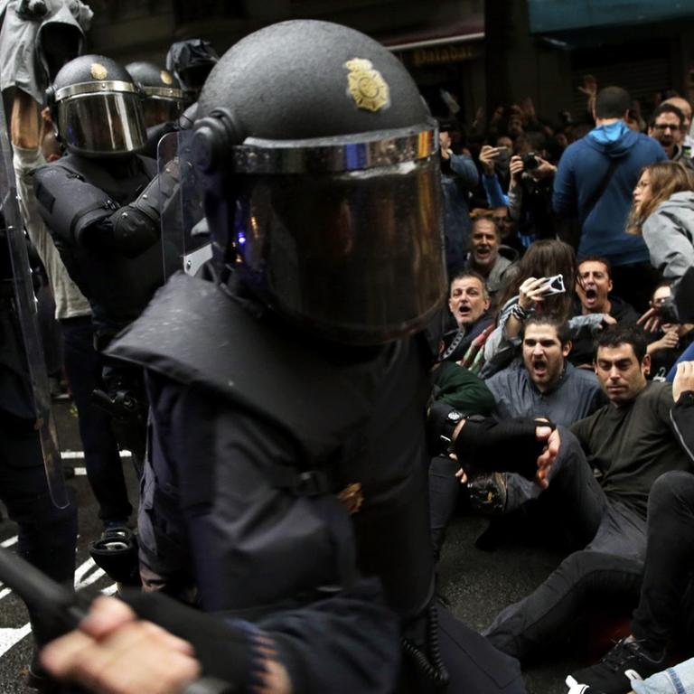 Ein spanischer Nationalpolizist geht mit seinem Schlagstock auf Befürworter des Katalonien-Referendums los, die sich auf die Straße gesetzt haben, am 01.10.2017 in Barcelona (Spanien)