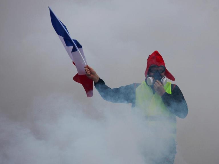 Ein Demonstrant der "Gelbwesten" mit einer französischen Flagge inmitten von Tränengas in Paris