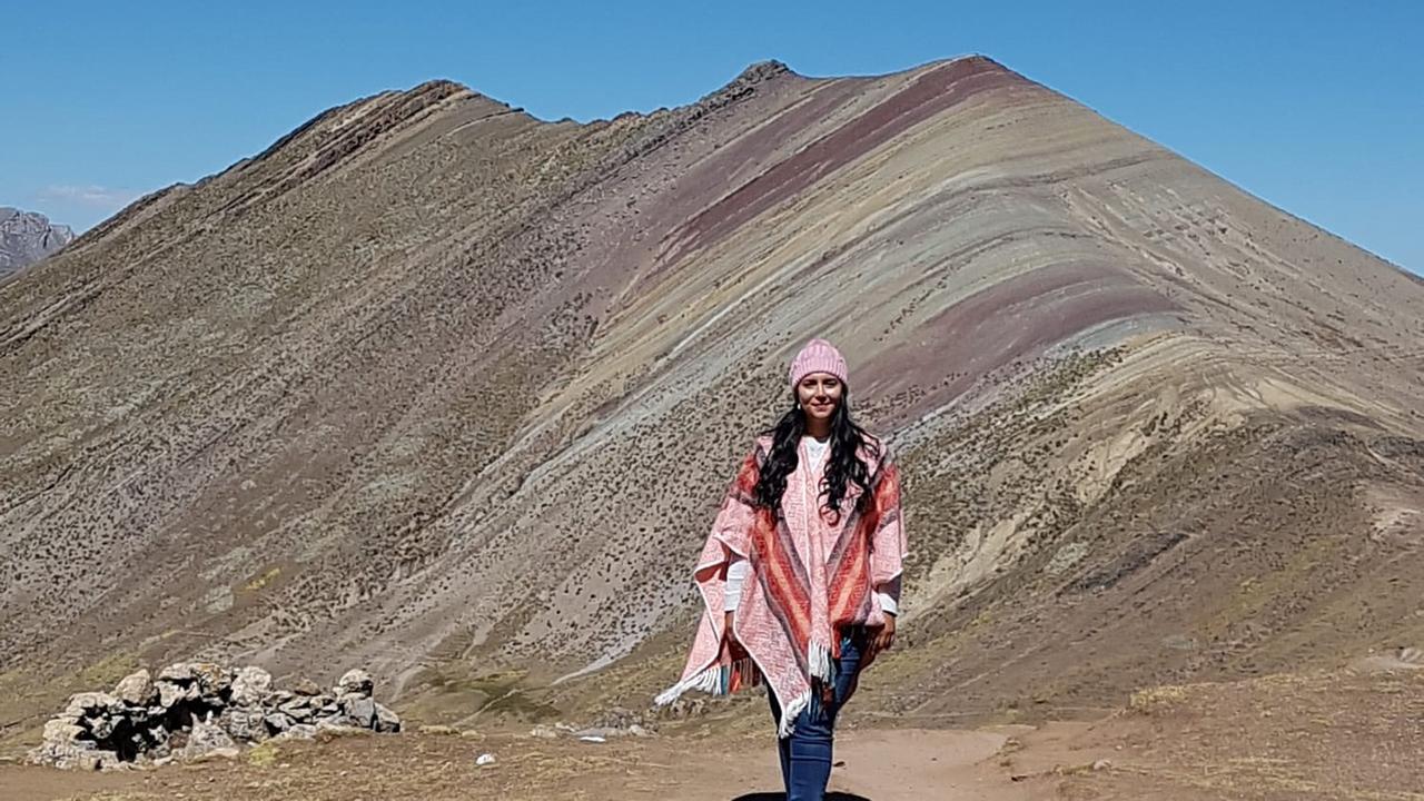 Hülya Al, mit rotem Poncho und rosa Mütze, geht in einem Gebirge spazieren.