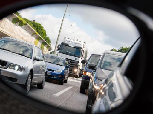 Autos und Lastwagen stehen am 20.06.2015 in Hamburg auf der Autobahn 7 bei Stellingen im Stau und sind dabei durch einen Rückspiegel zu sehen.