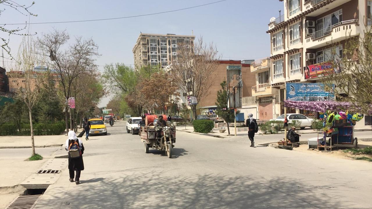 Auf einer von Wohnblocks gesäumten Straße in Kabul fahren vereinzelte Autos, am Rand laufen Menschen. 