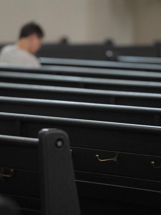 Ein einzelner Mensch sitzt in den ansonsten leeren Kirchenbänken.