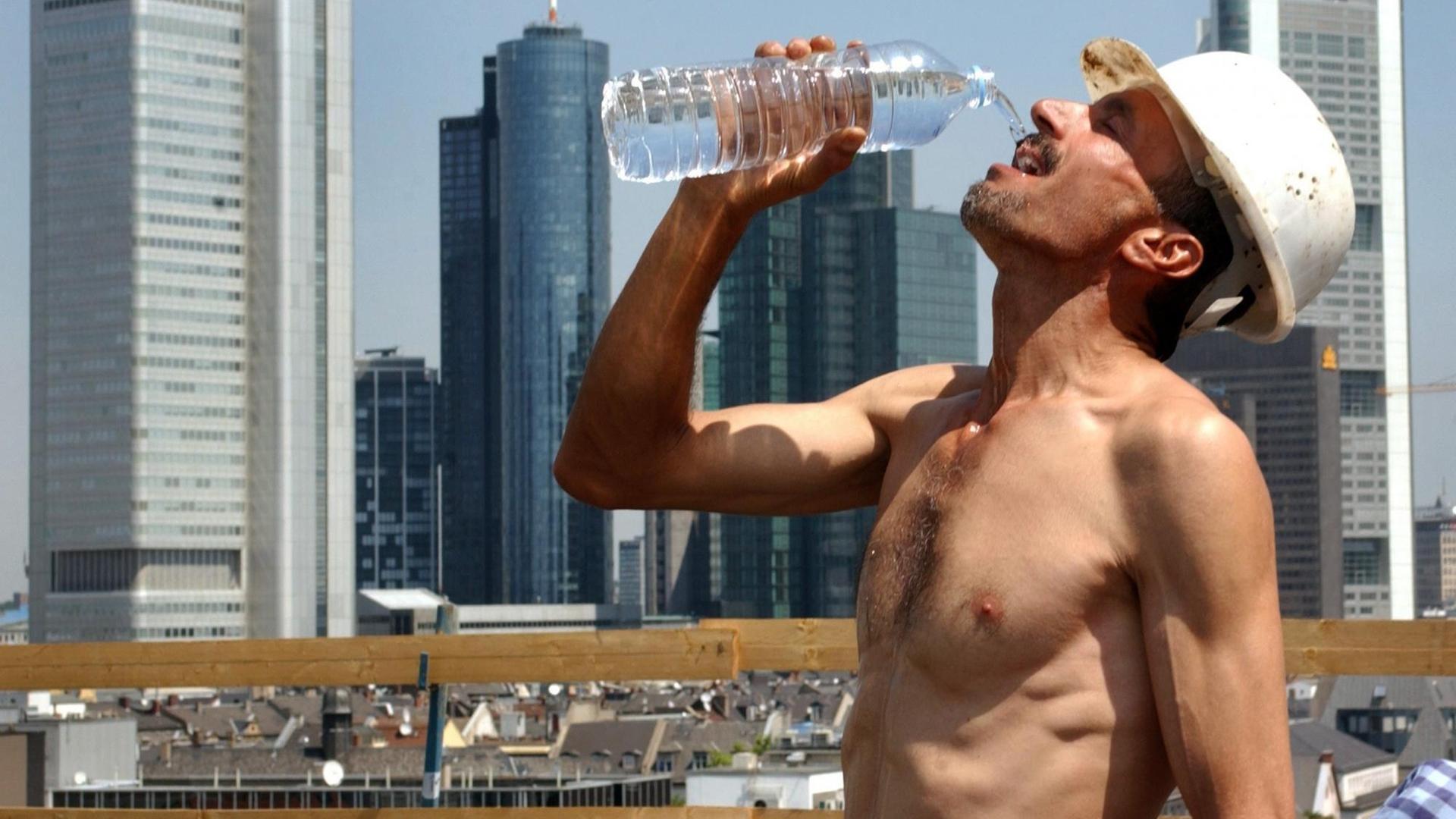 Bei sommerlicher Hitze erfrischt sich ein Bauarbeiter auf einer Baustelle vor der Frankfurter Skyline mit einem Schluck Wasser.