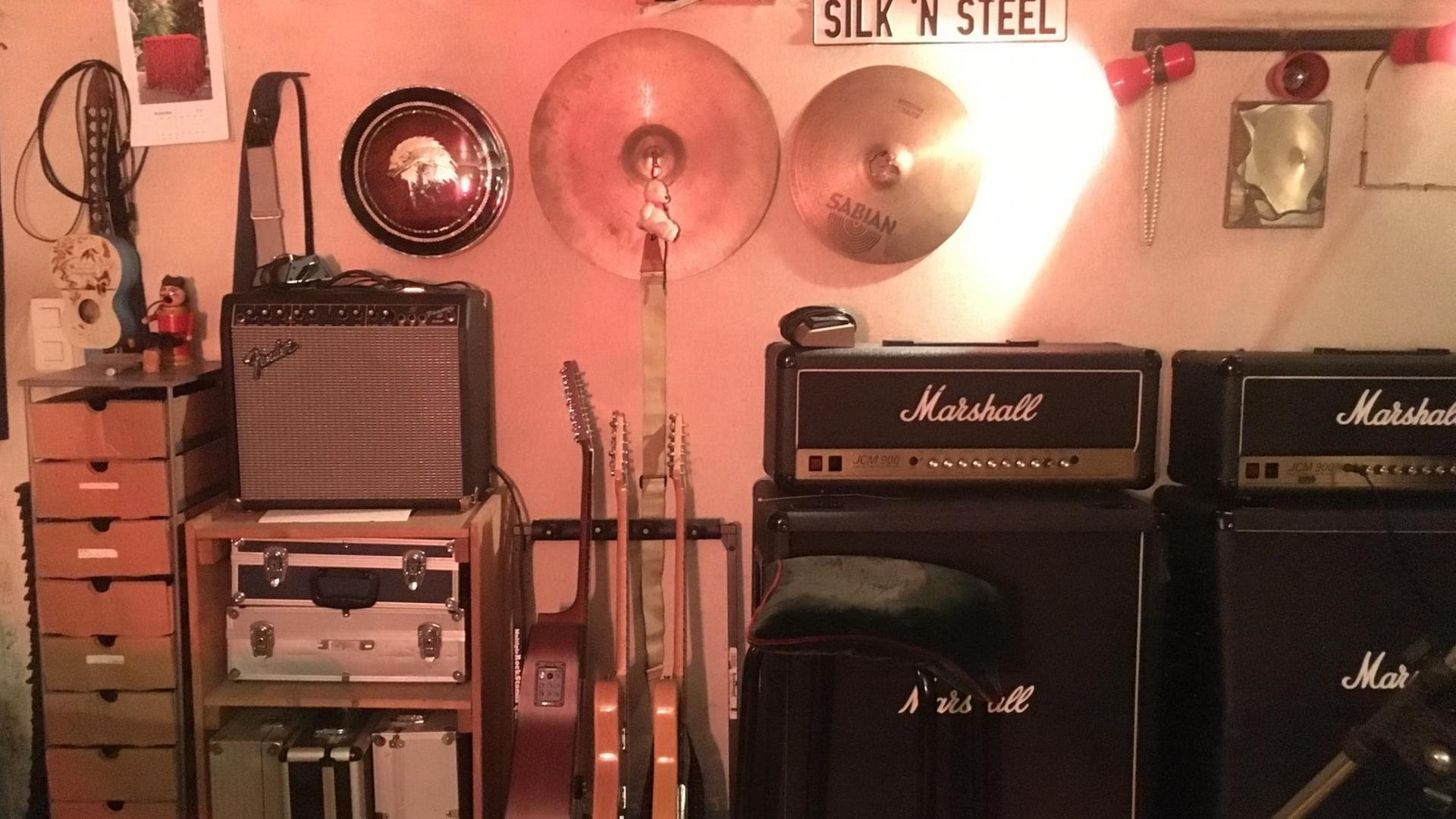 Proberaum - mehrere Verstärker und Gitarren stehen im Raum und Schlagzeugbecken und Kabel hängen an der Wand