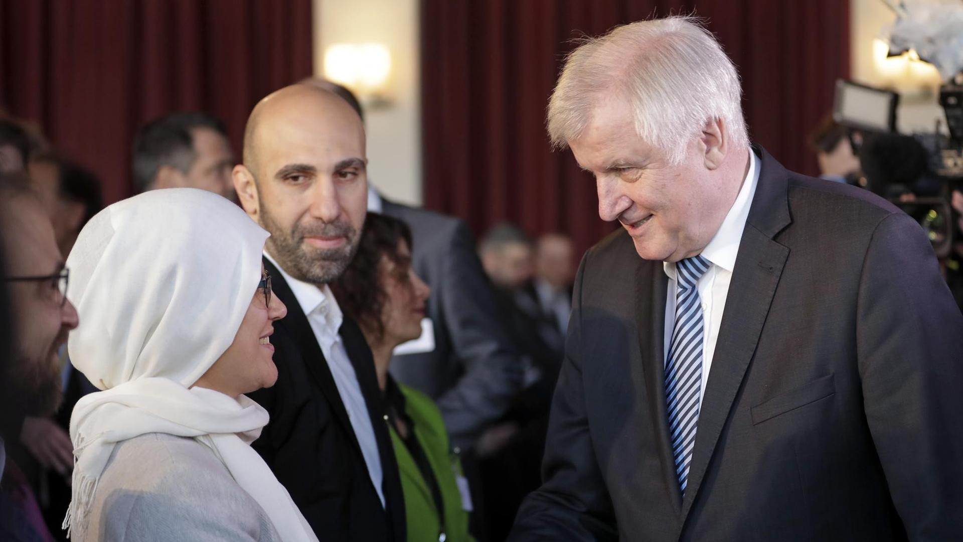 Bundesinnenminister Horst Seehofer schüttelt die Hand einer Frau, die ein weißes Kopftuch trägt.