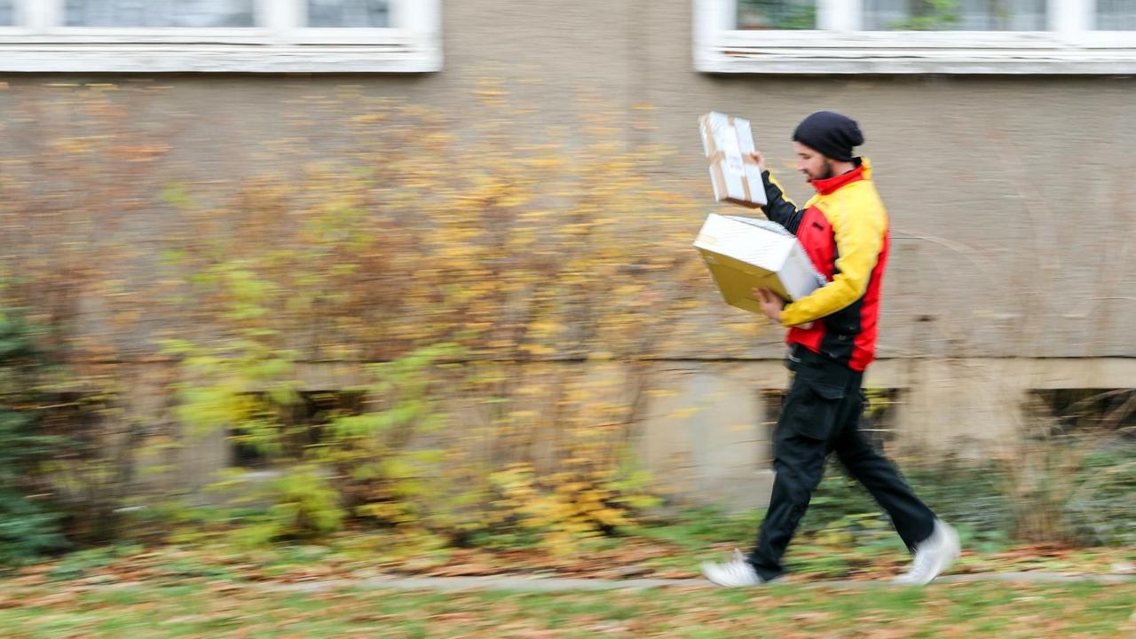 Ein DHL-Paketzusteller geht mit mehreren Sendungen zu einem Haus im Paulusviertel in Halle.