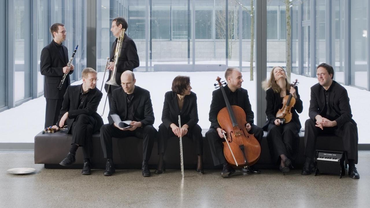 Die Musikerinnen und Musiker des E-Mex Ensemble stehen und sitzen in einer Halle