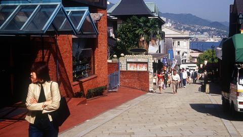 Touristen flanieren auf der Souvenirstraße bei Glover Garden mit Blick auf den Hafen von Nagasaki.