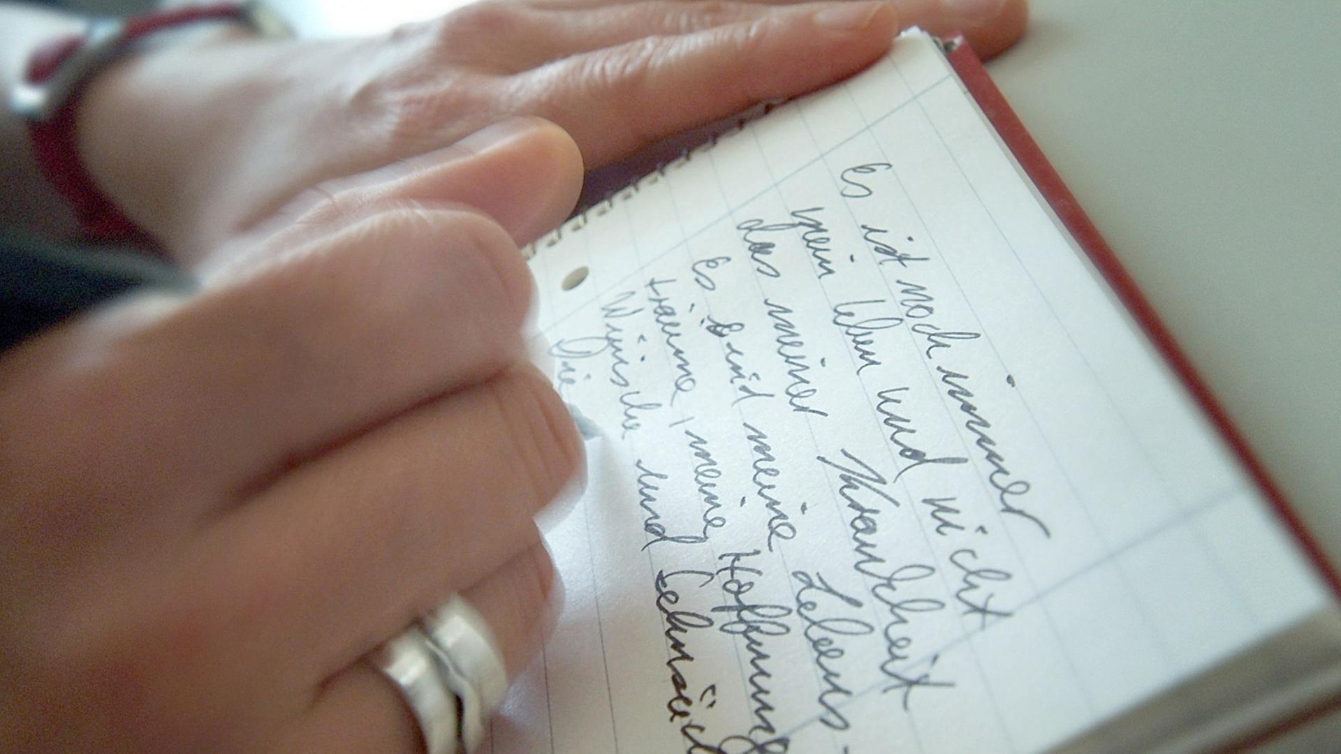 Eine Frau schreibt ihre Gedanken und Gefühle in einen Schreibblock.
