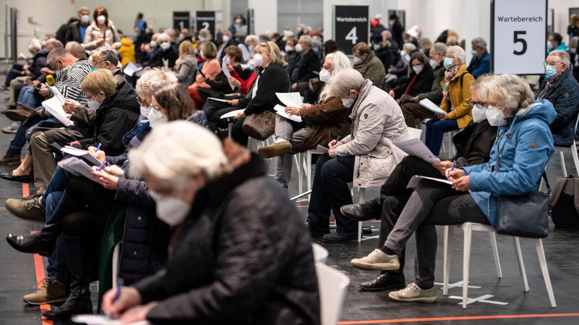 Viele Menschen warten mit Mund-Nasen-Bedeckung in einem Impfzentrum in Nordrhein-Westfalen.
