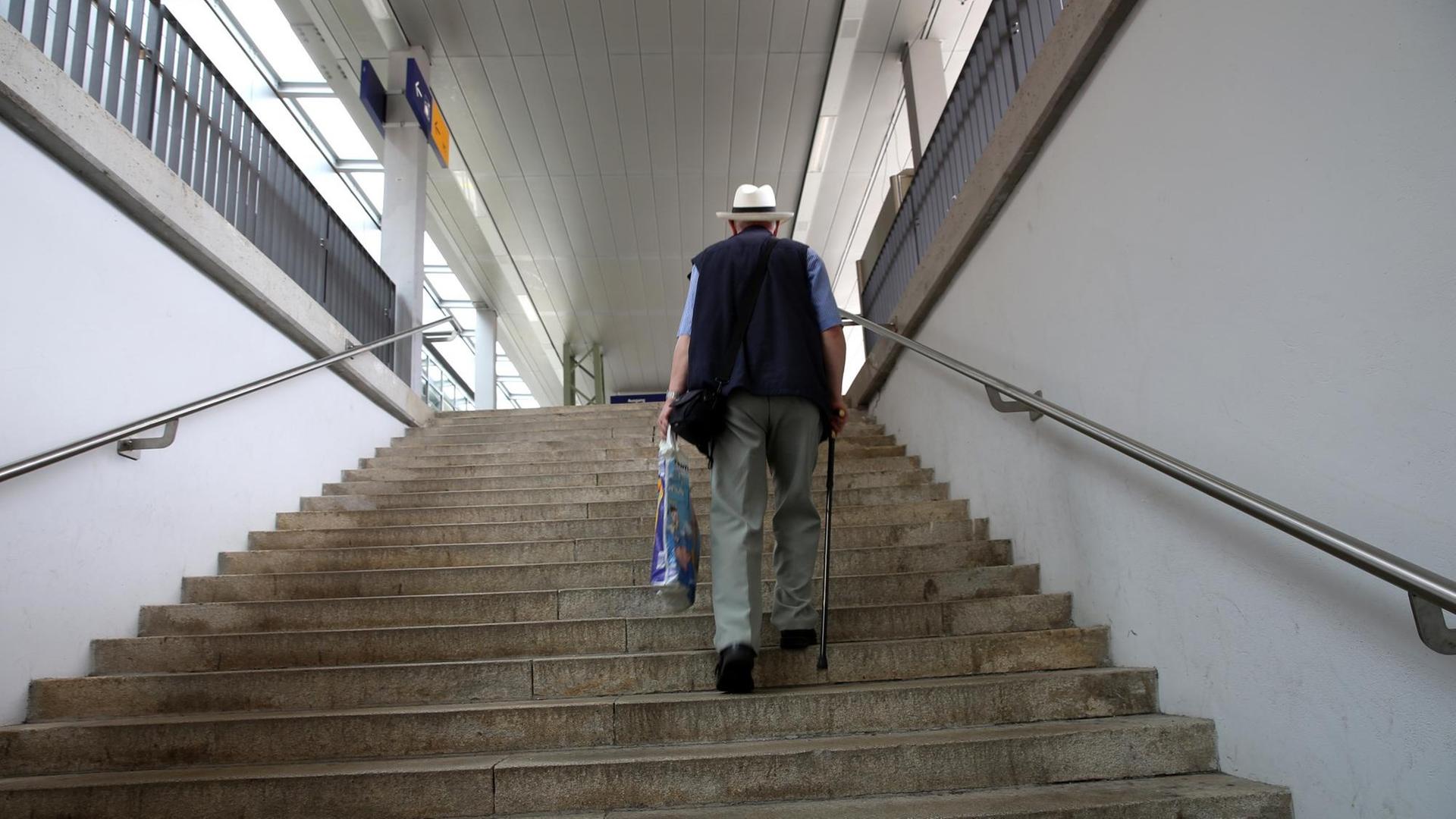 Ein älterer Herr mit Gehstock trägt eine Plastiktüte und steigt eine Treppe hoch.