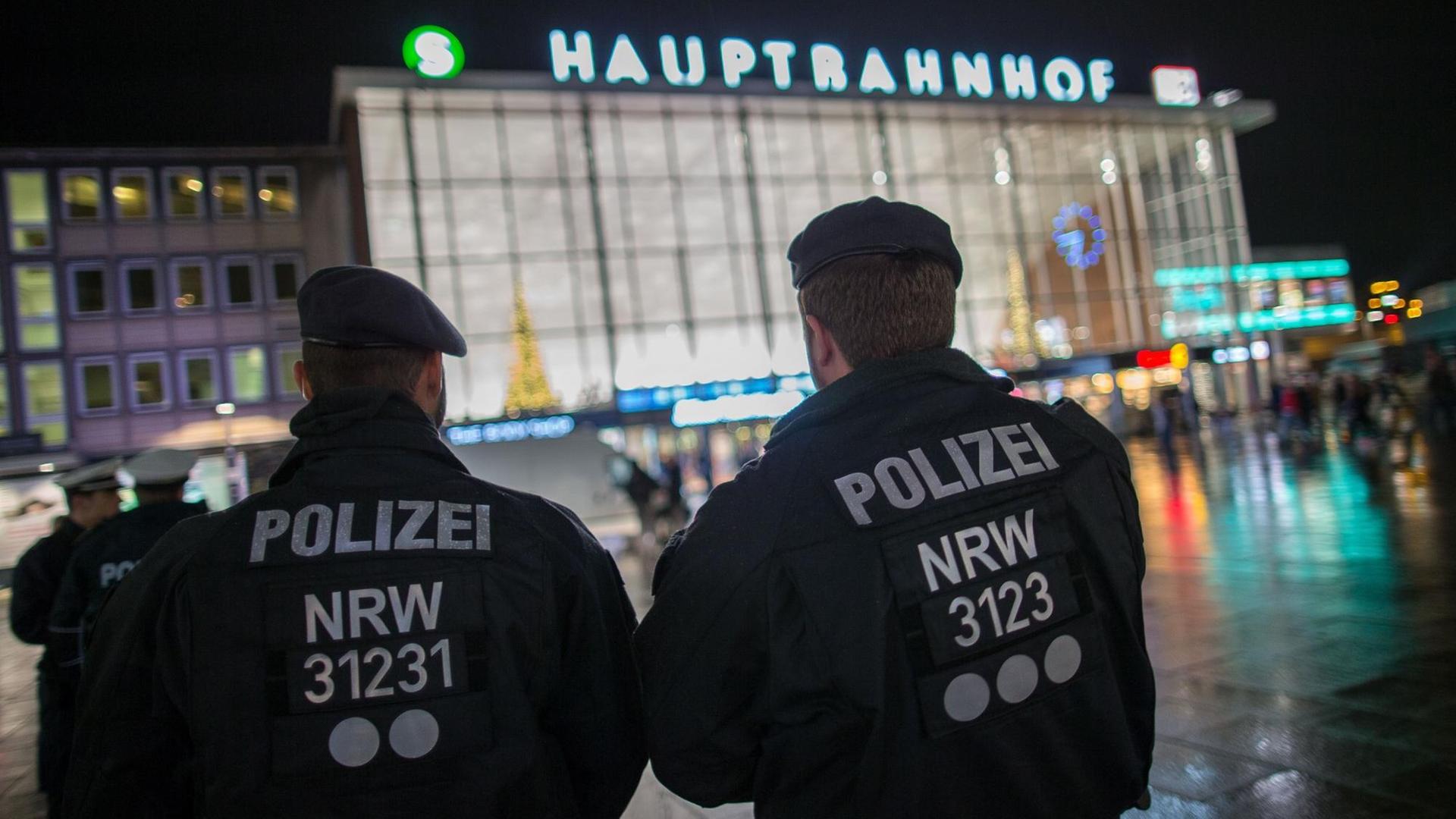 Polizisten stehen am Abend mit dem Rücken zur Kamera vor dem Kölner Hauptbahnhof.