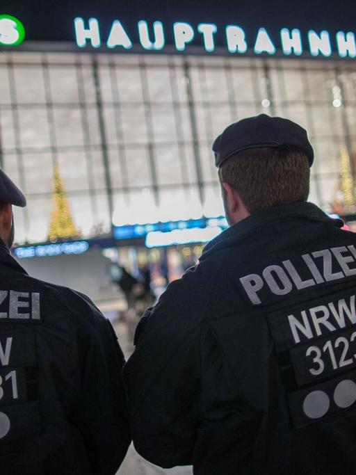 Polizisten stehen am Abend mit dem Rücken zur Kamera vor dem Kölner Hauptbahnhof.
