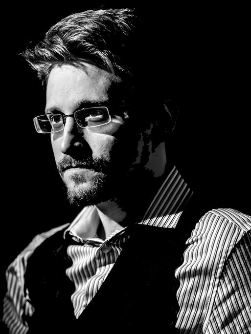 Edward Snowden blickt im halbdunkel und im Halbprofil stehend links am Betrachter vorbei.