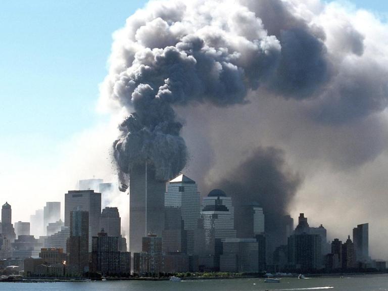 Dicker schwarzer Rauch tritt am 11.9.2001 aus den brennenden Türmen des World Trade Center. Wrack- und Gebäudeteile fliegen auf die Straße. Kurz zuvor waren zwei Flugzeuge hintereinander in die beiden Türme gerast.