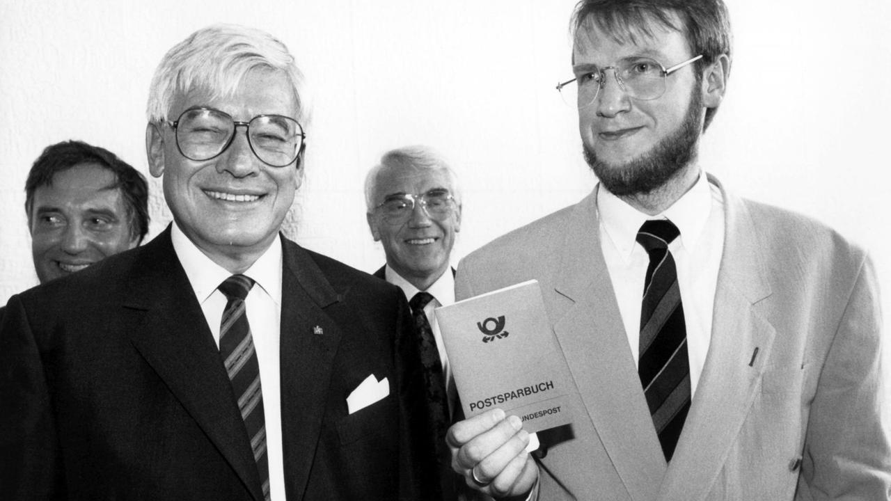 Die beiden deutschen Postminister Christian Schwarz-Schilling (links) und Emil Schnell (DDR) geben am 17.05.1990 bei der Eröffnung der ersten Postbank-Filiale am Alexanderplatz in Berlin die ersten Postsparbücher persönlich aus