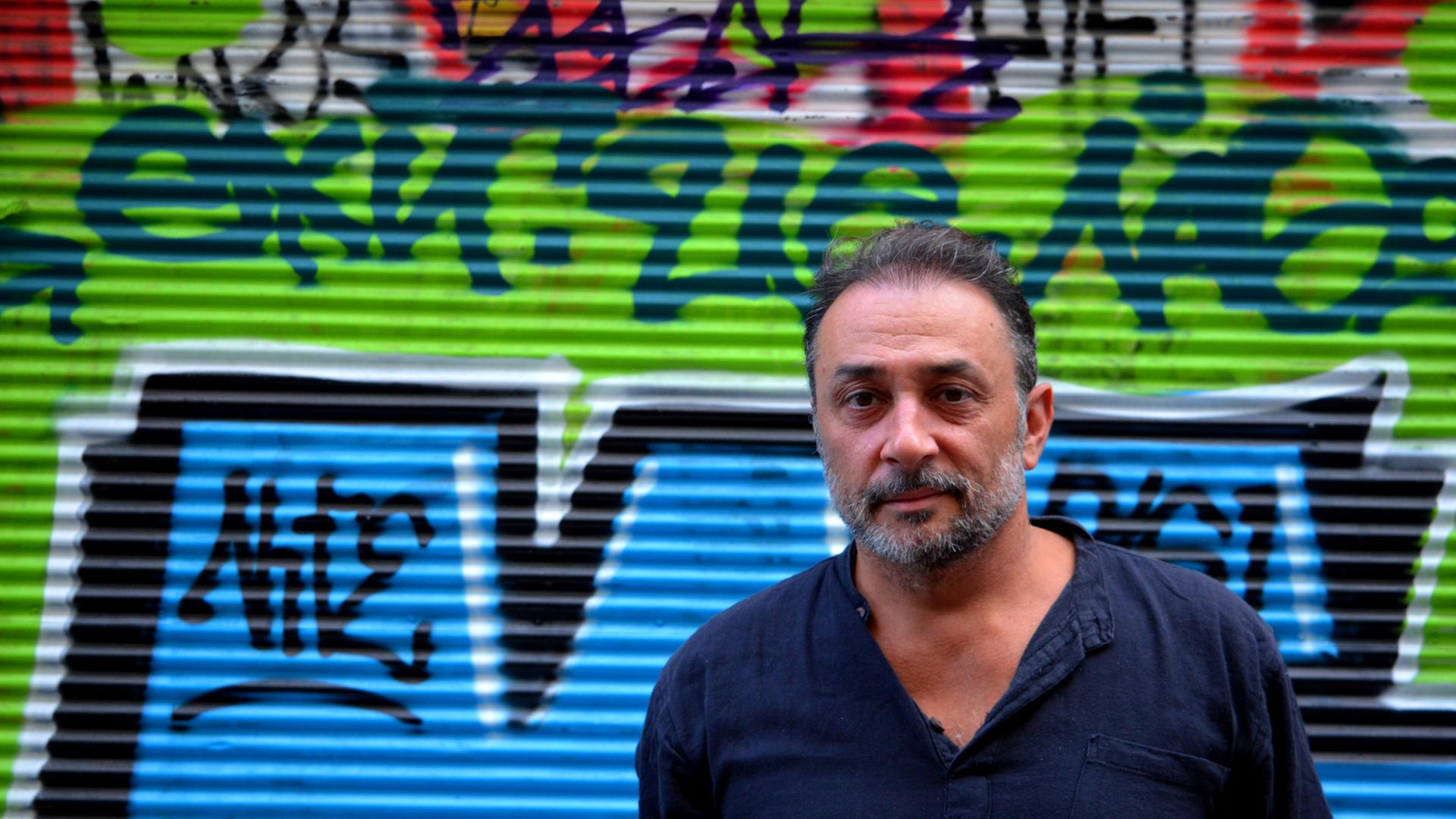 Der Schauspieler und Aktivist Vassilis Koukalani vor einem Graffiti