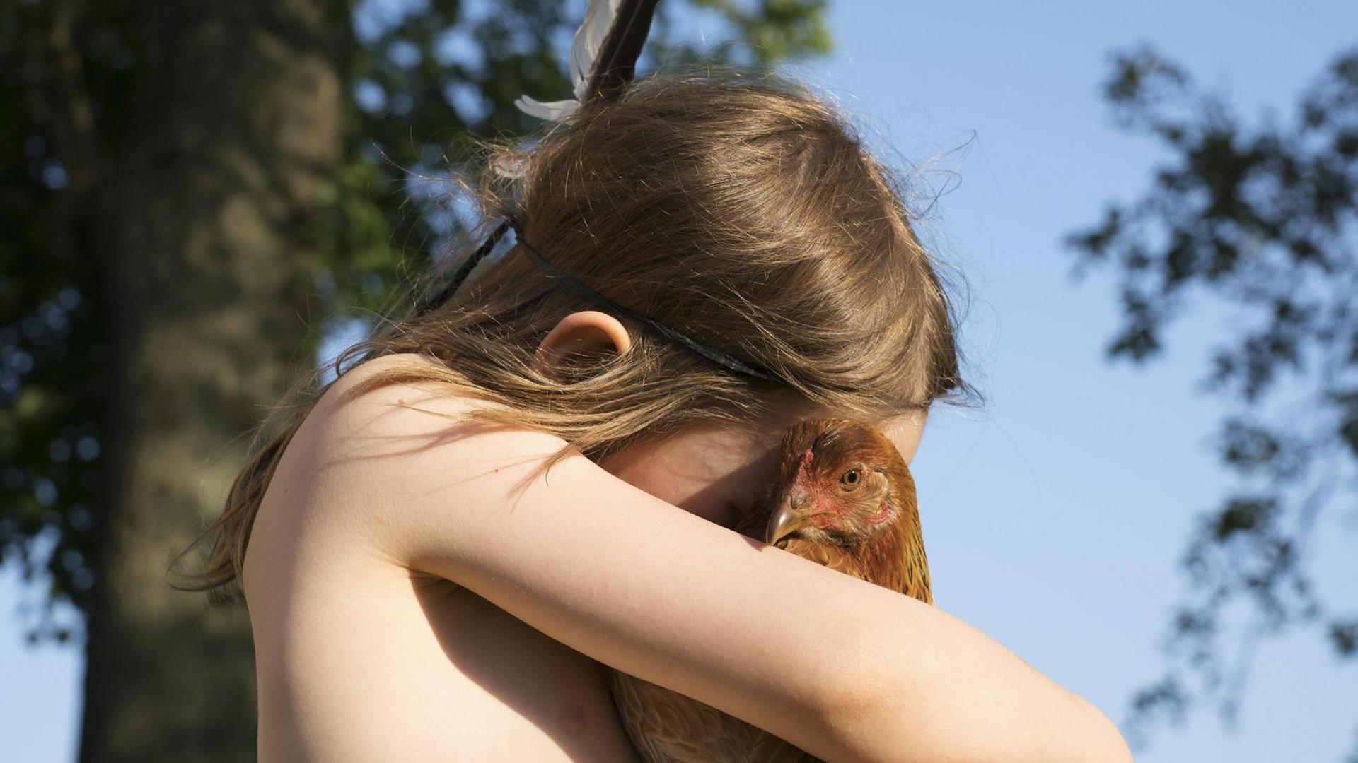 Ein Mädchen hält ein Huhn und umarmt es.