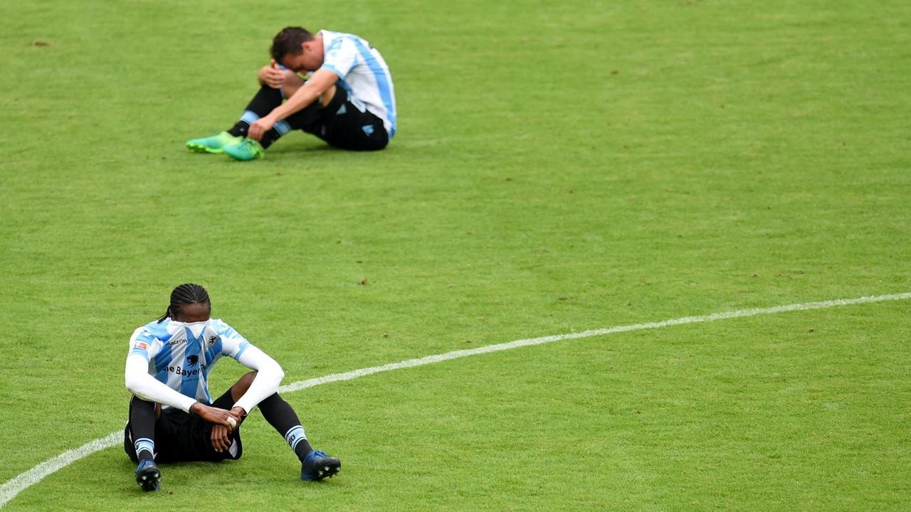 Die beiden Spieler sitzen enttäuscht auf dem Rasen, Ba hat das Trikot über das Gesicht gezogen.